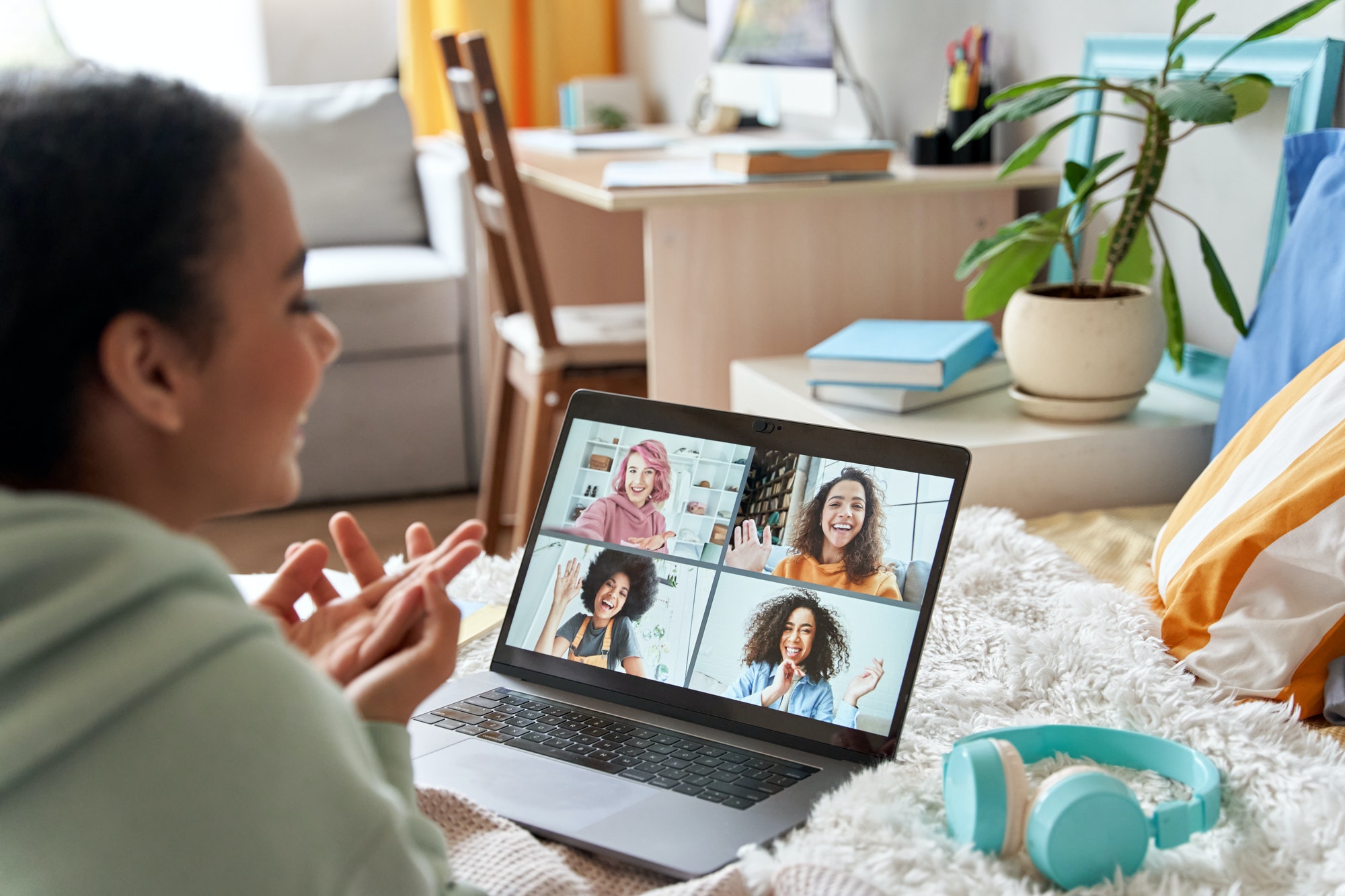 African teen girl talking with friends on distance video group call in bedroom.